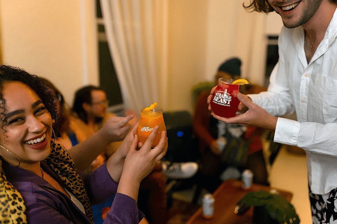 Two friends raising glasses of Strainge Beast hard kombucha and smiling